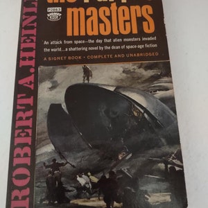 May include: A vintage paperback book cover with a dark brown background and a large, orange title: "The Puppet Masters". The cover features a black and white illustration of a large, flying saucer landing on a beach with people running away.