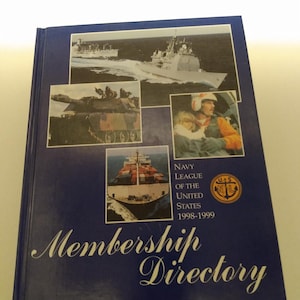 May include: A blue book with the title "Membership Directory" and the text "Navy League of the United States 1998-1999". The book cover features images of a ship, a tank, a cargo ship, and a person in a flight suit.