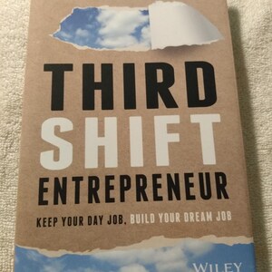 May include: A brown book with a torn paper design on the cover. The title is "Third Shift Entrepreneur" with the subtitle "Keep Your Day Job, Build Your Dream Job". The author is Todd Connor and the book is published by Wiley.