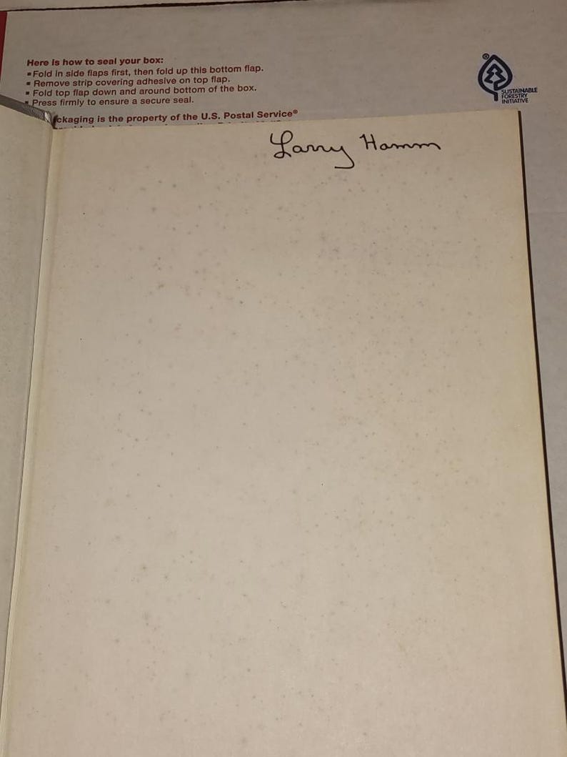 Puede incluir: P&aacute;gina de libro abierta con el nombre manuscrito "Larry Hamm". Las instrucciones impresas para sellar una caja est&aacute;n en la parte superior izquierda. El logotipo del Servicio Postal de EE. UU. es visible. El logotipo de la Iniciativa Forestal Sostenible est&aacute; en la esquina superior derecha.