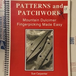 May include: A spiral-bound instructional book titled Patterns and Patchwork Mountain Dulcimer Fingerpicking Made Easy by Sue Carpenter. The cover is red with white text and features a black and white photograph of two mountain dulcimers.