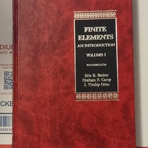 May include: A red hardcover book titled "Finite Elements, An Introduction, Volume I." The book's cover features gold lettering and a black rectangular label with the authors' names. The book has a textured, reddish-brown cover.