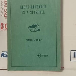 May include: A light green softcover book titled Legal Research in a Nutshell by Morris L. Cohen. The cover features a dark green illustration of a walnut shell in the center and the West Publishing Co. logo at the bottom.