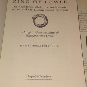 K&ouml;nnte beinhalten: Ein Buch mit dem Titel Ring of Power: The Abandoned Child, the Authoritarian Father, and the Disempowered Feminine, A Jungian Understanding of Wagner's Ring Cycle von Jean Shinoda Bolen, M.D., mit einer schwarz-wei&szlig;en Ouroboros-Illustration.