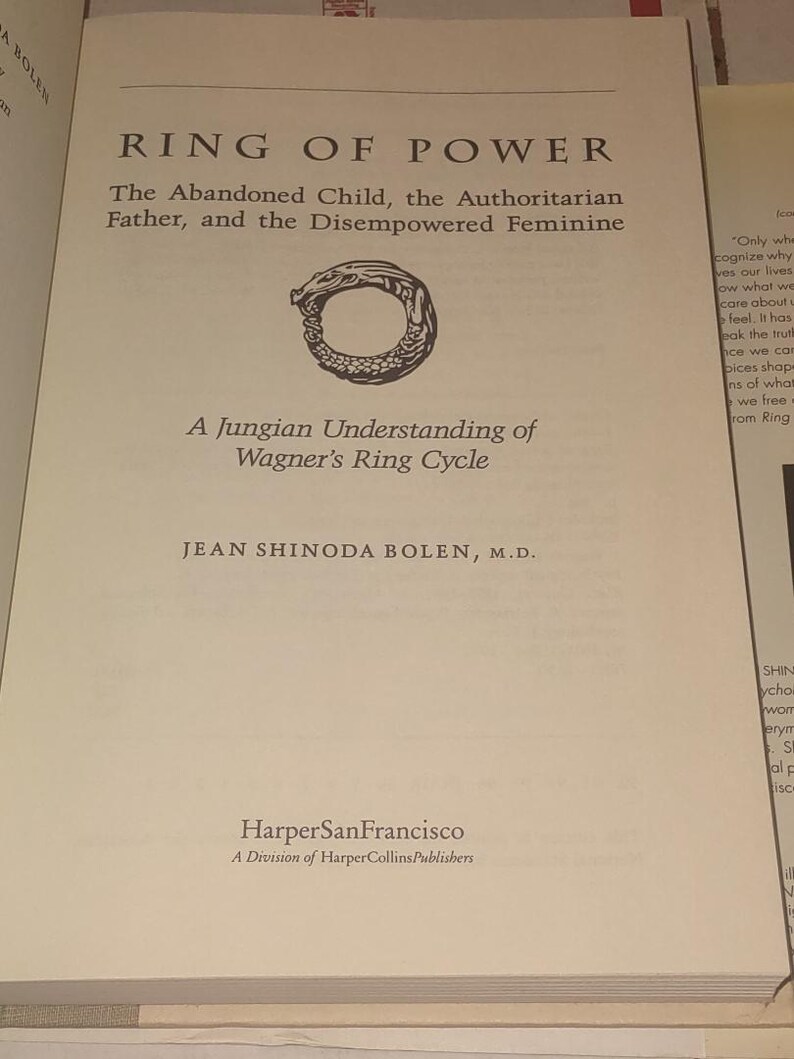K&ouml;nnte beinhalten: Ein Buch mit dem Titel Ring of Power: The Abandoned Child, the Authoritarian Father, and the Disempowered Feminine, A Jungian Understanding of Wagner's Ring Cycle von Jean Shinoda Bolen, M.D., mit einer schwarz-wei&szlig;en Ouroboros-Illustration.