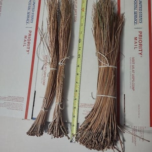 May include: Three bundles of dried pine needles tied together with twine. The bundles are approximately 12 inches long and are arranged on a white surface. The bundles are next to a measuring tape that shows the length of the bundles.