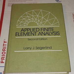 May include: A green textbook titled "APPLIED FINITE ELEMENT ANALYSIS, Second Edition" by Larry J. Segerlind. The book has a white geometric design on the cover and is on a white surface.