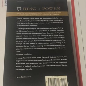 K&ouml;nnte beinhalten: Die R&uuml;ckseite des Buches Ring of Power von Jean Shinoda Bolen, M.D. Der schwarze Einband zeigt goldenen Text, eine Zusammenfassung der psychologischen Themen des Buches, den Verlag HarperSanFrancisco und einen Strichcode mit ISBN 0-06-250086-4.