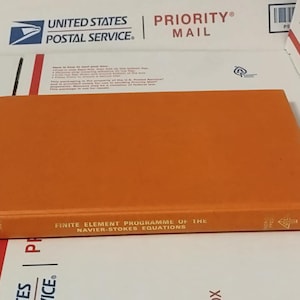 May include: An orange hardcover book titled "Finite Element Programme of the Navier-Stokes Equations." The book is lying on a white surface with "United States Postal Service" and "Priority Mail" markings.