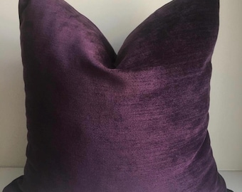 May include: A deep purple velvet cushion with a soft, textured surface. The cushion is square shaped and has a simple design.