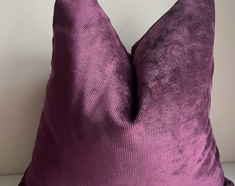 May include: A deep purple velvet cushion with a textured, ribbed surface. The cushion is square shaped and has a simple, elegant design.