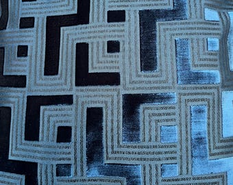 May include: Close-up of a cushion with a geometric pattern. The design features a repeating pattern of squares and rectangles in shades of blue, grey, and black. The fabric has a textured appearance, adding depth to the design.