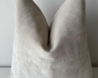May include: A large, square, light beige pillow with a soft, textured surface. The pillow is made of a plush material and has a slightly wrinkled appearance. The pillow is a neutral color and would complement various home decor styles.