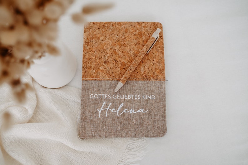May include: A cork and linen journal with a white pen and the text "Gottes geliebtes Kind Helena" in white lettering.