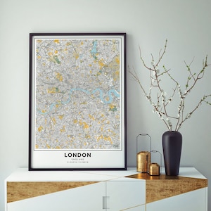 Peut inclure: Une impression encadr&eacute;e noire d'une carte de Londres, en Angleterre. La carte est de style vintage avec des lignes jaunes et grises. L'impression est accroch&eacute;e &agrave; un mur blanc au-dessus d'une commode dor&eacute;e et blanche.