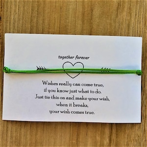 May include: A green friendship bracelet with an arrow and heart design. The card reads "together forever" and includes the text "Wishes really can come true, if you know just what to do. Just tie this on and make your wish, when it breaks, your wish comes true."