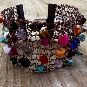 Op de afbeelding: Een koperen draad armband met een verscheidenheid aan kleurrijke stenen en kralen. De armband is geweven in een mesh-patroon en heeft een sluiting.