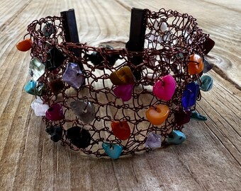 May include: A copper wire bracelet with a variety of colorful stones and beads. The bracelet is woven in a mesh pattern and has a clasp closure.