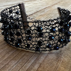 May include: A black choker necklace with a delicate wire mesh design and black beads. The necklace has a clasp closure.