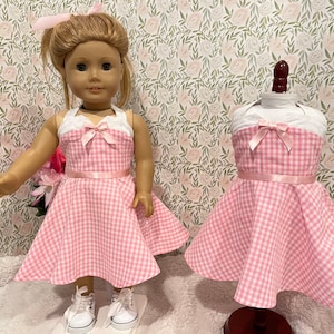 Pode incluir: Um vestido rosa e branco xadrez para boneca, com um top branco de cabresto e um la&ccedil;o rosa. O vestido &eacute; exibido em uma boneca e em um manequim. A boneca est&aacute; usando t&ecirc;nis brancos e tem um la&ccedil;o rosa combinando no cabelo.