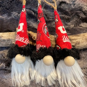 May include: Three red and black gnomes with white beards. The gnomes are wearing hats with the University of Utah logo and the words "Utah Utes".