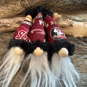 May include: Three gnomes with white beards and black fur hats. The hats are decorated with different college logos: Florida State, Florida, and Seminole State.