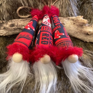 May include: Three red and black gnome ornaments with white beards. The gnomes are wearing hats with the Boston Red Sox logo and the words "1901", "Red Sox", and "Cool Baseball".