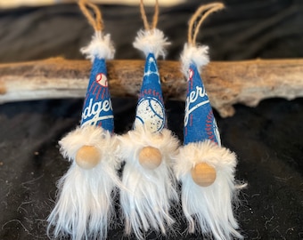 Puede incluir: Tres adornos de gnomo azul y blanco con barbas de piel blanca. Los gnomos llevan sombreros con el logotipo de los Dodgers de Los Angeles y diseños de béisbol.