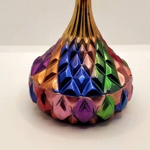May include: A colorful, geometric, ceramic trinket box with a gold top. The box is decorated with a diamond pattern in shades of red, orange, green, blue, and purple.