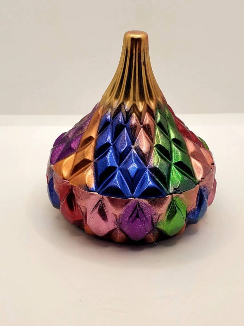 May include: A colorful, geometric, ceramic trinket box with a gold top. The box is decorated with a diamond pattern in shades of red, orange, green, blue, and purple.