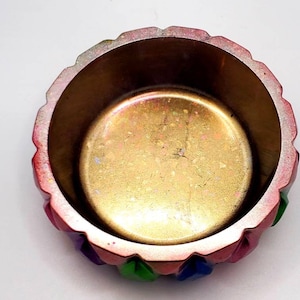 May include: A small, round, decorative bowl with a gold interior and a multi-colored exterior. The bowl has a scalloped rim and is decorated with green, blue, and pink accents.