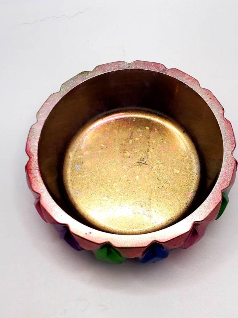 May include: A small, round, decorative bowl with a gold interior and a multi-colored exterior. The bowl has a scalloped rim and is decorated with green, blue, and pink accents.