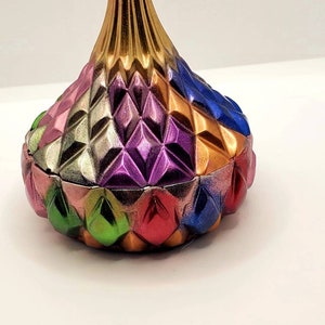 May include: A colorful, geometric, ceramic trinket box with a gold top. The box is shaped like a Hershey's Kiss and has a diamond pattern.
