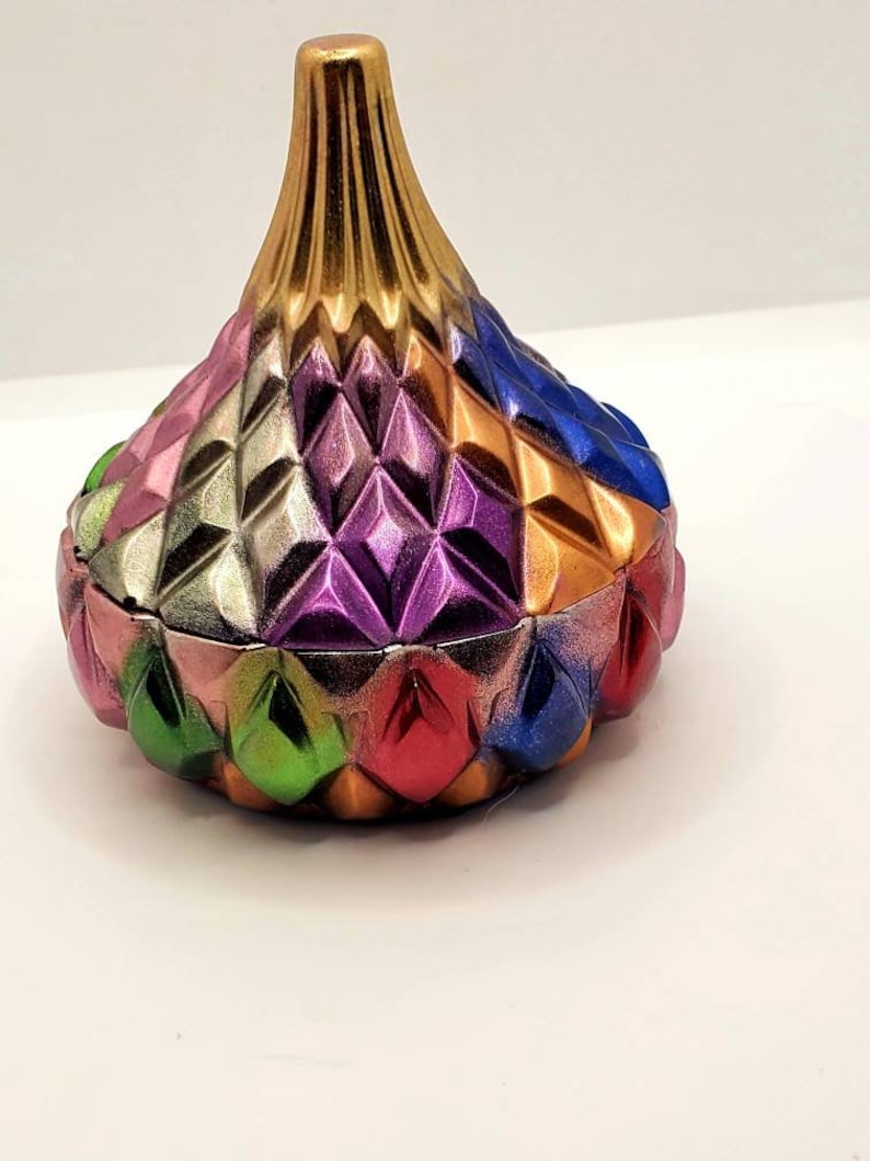 May include: A colorful, geometric, ceramic trinket box with a gold top. The box is shaped like a Hershey's Kiss and has a diamond pattern.