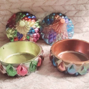 May include: Two small, round, iridescent trinket boxes with lids. The lids are decorated with a geometric pattern of colorful, iridescent triangles. The boxes are open and the inside of each box is a different color. One box is green and the other is brown.