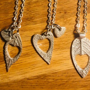 May include: Five silver necklaces with different pendants. The pendants include a sunflower, a heart with a smaller heart charm, a leaf with a heart cut-out, a leaf with a heart cut-out, and a leaf.