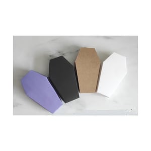 Könnte beinhalten: Vier sargförmige Schachteln in einer Reihe. Die Schachteln sind in verschiedenen Farben: Lavendel, Schwarz, Braun und Weiß. Die Schachteln sind aus Pappe und haben eine matte Oberfläche. Die Schachteln sind leer und bereit zum Befüllen.