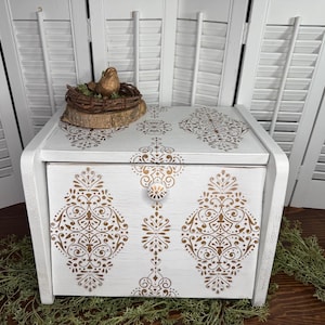 May include: White bread box with a gold damask pattern. The box has a hinged lid and a small knob on the front.