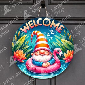 May include: Round welcome sign featuring a sleeping gnome in a flamingo floatie. The sign has the word "WELCOME" in colorful letters. The gnome wears a striped hat and is surrounded by tropical plants and flowers.