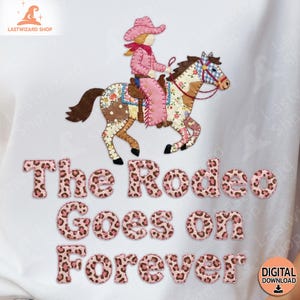 Peut inclure: T-shirt blanc avec une cowgirl rose chevauchant un cheval patchwork. Le texte "The Rodeo Goes on Forever" est en police léopard rose. Le logo Lastwizard Shop est en haut à gauche.