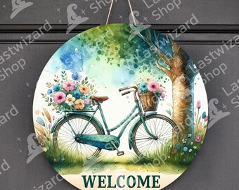 May include: A round wooden sign with a watercolor painting of a bicycle with flowers in the basket. The bicycle is green and has a white basket. The background is a watercolor painting of a tree and flowers. The sign says "WELCOME" in green letters.