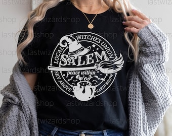 Può includere: Maglietta nera con una grafica bianca di un cappello da strega, una scopa, un calderone e pipistrelli. La grafica dice "Local Witches Union Salem" e "Peace Within, Sky Above, Earth Below".