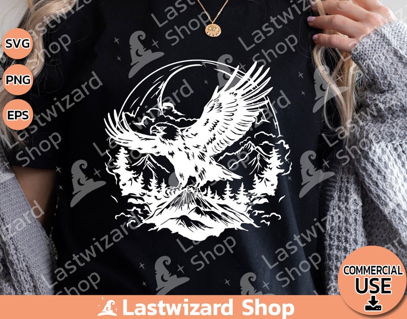 May include: A black t-shirt with a white graphic of an eagle soaring over a mountain range. The eagle is in flight with its wings spread wide. The mountain range is in the background and is made up of several peaks. The graphic is surrounded by a circle of clouds.