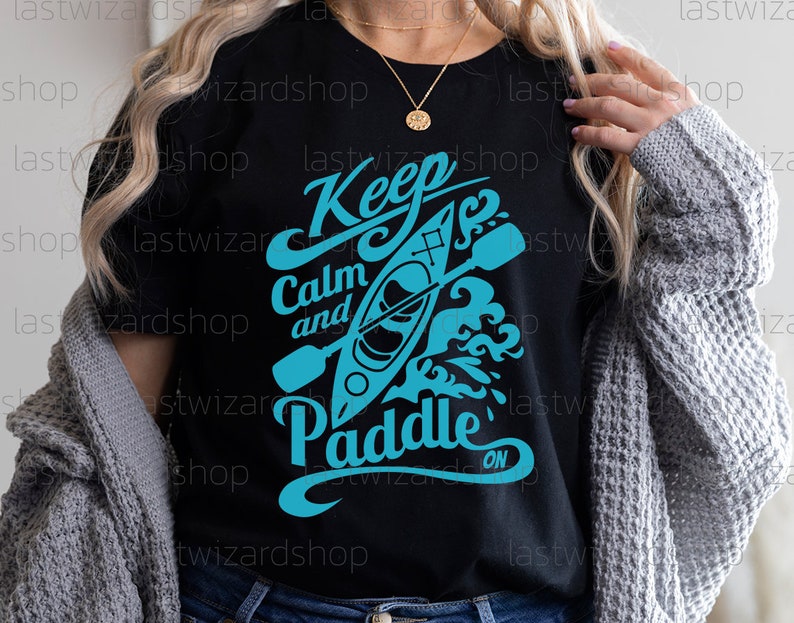 May include: Black t-shirt with a blue graphic design that says "Keep Calm and Paddle On". The graphic features a kayak with paddles and waves.