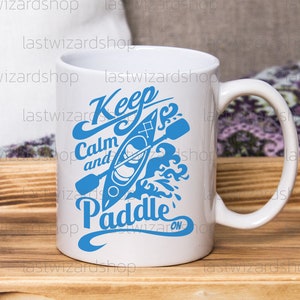 May include: White ceramic mug with a blue graphic that says "Keep Calm and Paddle On" with a stylized image of a kayak and paddle.