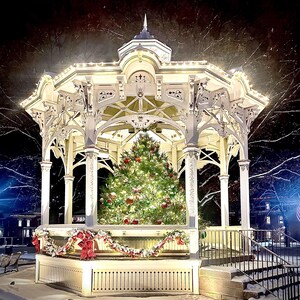 May include: A white gazebo decorated with Christmas lights and a decorated Christmas tree inside. The gazebo has ornate architectural details and is surrounded by snow. A garland with red bows adorns the front.