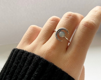 May include: A silver ring with a crescent moon design and a white opal stone in the center.