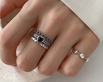 May include: A set of three silver rings with a black heart charm. The rings are stacked on a finger and feature intricate designs.