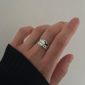 May include: A silver ring with a unique, slightly curved, rectangular design.