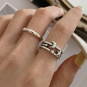 May include: A set of three silver rings featuring a crescent moon and stars. The rings are stacked on a finger.